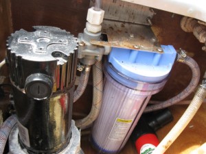 Image: Black cylinder on the left is the electric motor for the desalinator. On the right is its prefilter, both inside the watermaker cabinet.